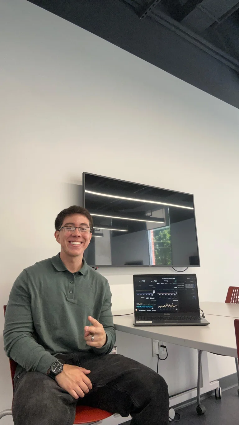 Freddy Flores smiling beside his laptop in a green shirt